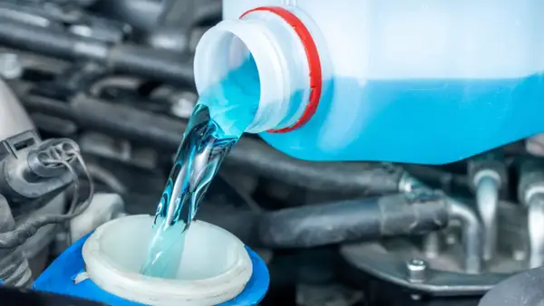 Blaues Scheibenwischwasser wird aus einem Behälter in den Einfüllstutzen gegossen.
