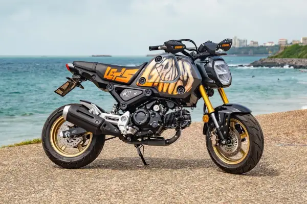 Niestandardowe malowanie baku motocykla z motywem płomieni i napisem "LET'S GO" na tle morza.
