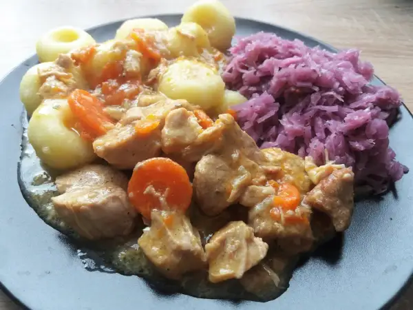 Pyszne duszenie z mięsa i marchewki, podane z kluskami i czerwoną kapustą.