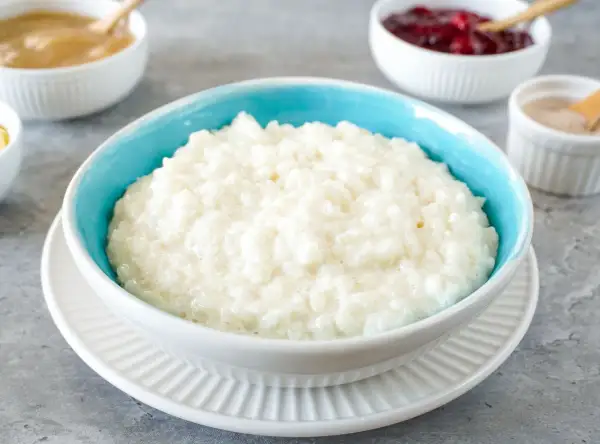 Cremiger Milchreis im blauen Schüsselchen, perfekt für ein einfaches Milchreis Rezept. Dazu Apfelmus und Kirschen.