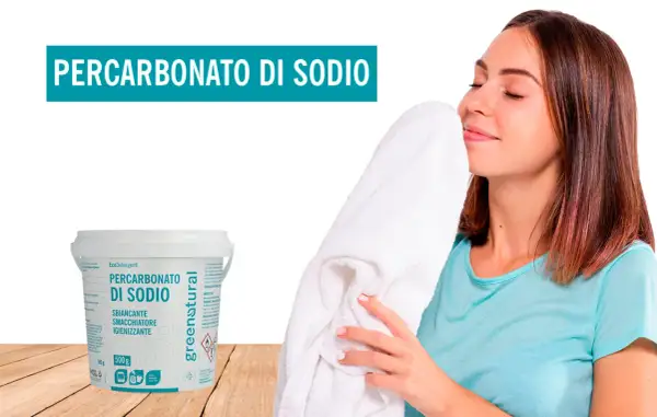 Donna annusa un asciugamano bianco fresco, accanto a un contenitore di percarbonato di sodio. Il percarbonato si può usare sui colorati per un bucato impeccabile.