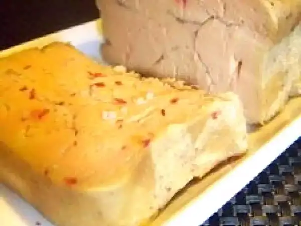 Deux blocs de foie gras sur une assiette blanche. L'un est parsemé de sel et de piment rouge, prêt pour une recette de foie gras au sel sans cuisson.