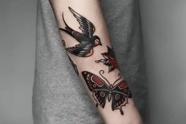 Tatuaż w stylu old school na przedramieniu: jaskółka, motyl i róża.