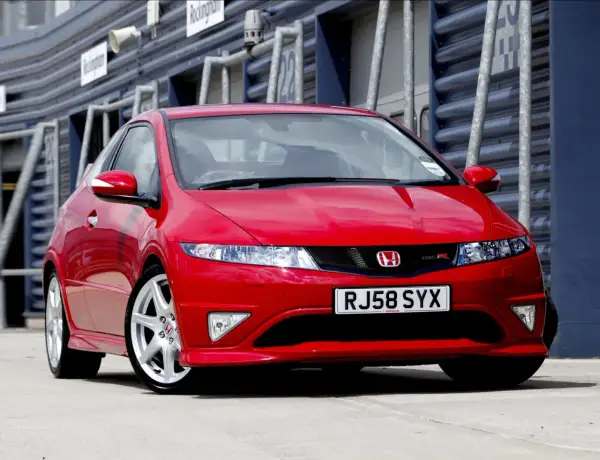 Czerwony Honda Civic Type R, wyglądający jak futurystyczne UFO, zaparkowany na torze wyścigowym.
