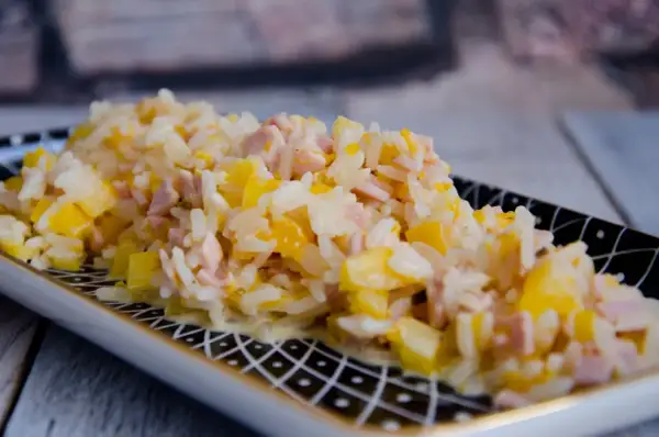 Reissalat mit Mandarinen und Schinken, cremig und fruchtig, auf einem dekorativen Teller serviert.