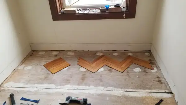 Wooden floor planks laid in a herringbone pattern on a subfloor, tools nearby. This is part of a project on how to level floor.