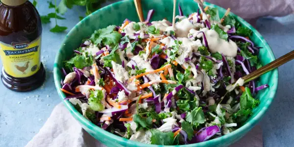En fräsch kycklingsallad med rödkål, morötter och grönkål, toppad med en krämig dressing. En flaska kycklingfond syns i bakgrunden.