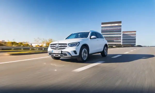 Biały Mercedes GLC 200 jedzie po pustej drodze, w tle nowoczesne budynki biurowe.