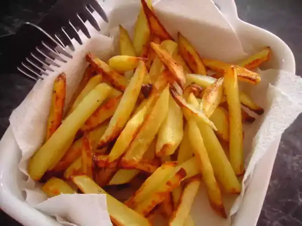 Un plat blanc rempli de délicieuses frites au four, dorées et croustillantes, prêtes à être dégustées. Une fourchette est posée sur le bord.