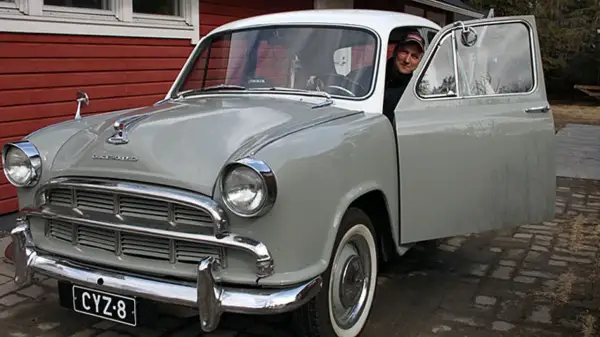 Man ler vid ratten i en grå Morris Oxford med öppen dörr.