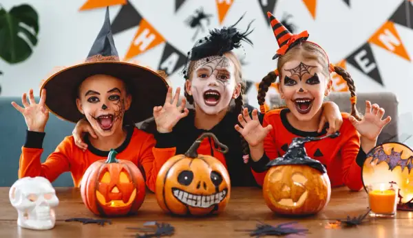 Tre barn med läskig ansiktsmålning och halloween-kostymer njuter av en halloween fest med pumpor och dekorationer.