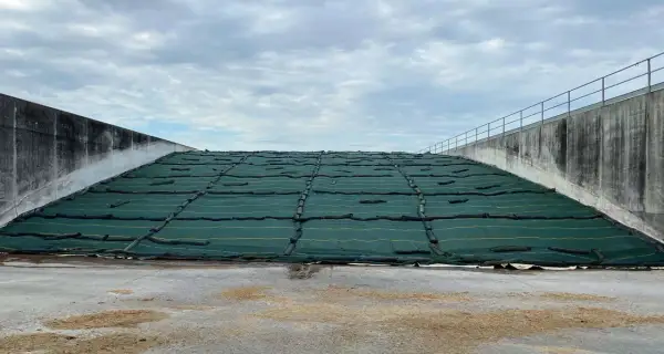 Ampia trincea agricola coperta da telo verde, con pareti in cemento e cielo nuvoloso.