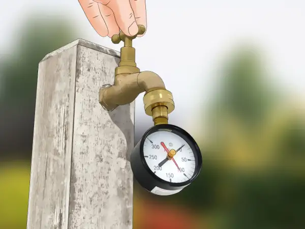 Mano girando la llave de un grifo de latón conectado a un manómetro que mide la presión en el agua.