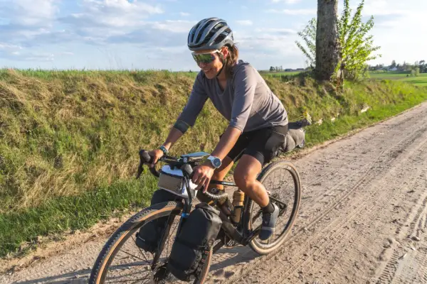 Kobieta w kasku i okularach przeciwsłonecznych jedzie na rowerze po piaszczystej drodze. To przygoda z rowerem w okolicach Gdańska.