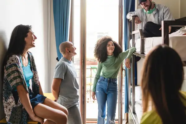 Grupa młodych ludzi rozmawia w pokoju z łóżkami piętrowymi. To idealny przykład, jak działa couchsurfing co to – wspólne podróże i poznawanie nowych ludzi.