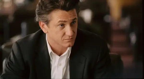 Sean Penn w czarnym garniturze i białej koszuli, wygląda jakby zastanawiał się nad kolejną rolą w swoich filmach.