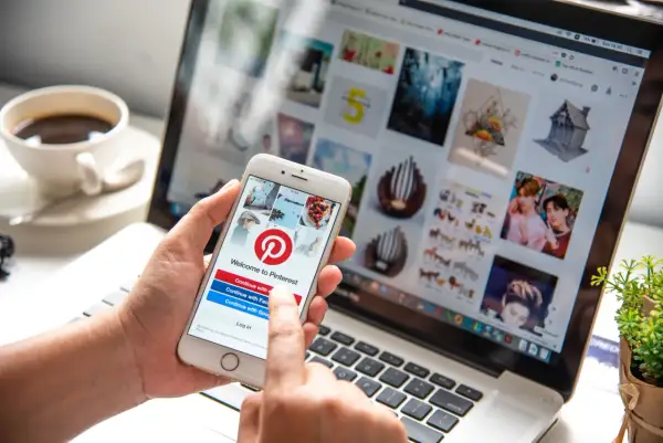 Osoba korzysta z telefonu z aplikacją Pinterest, sprawdzając, czy aplikacja Pinterest jest darmowa. Na ekranie telefonu widnieje logo Pinterest i opcje logowania.