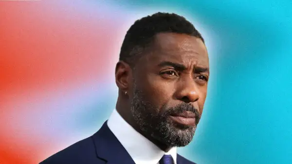 Idris Elba arbore une barbe grise stylée, un modèle barbe dégradé impeccable, sur fond dégradé rouge et bleu.
