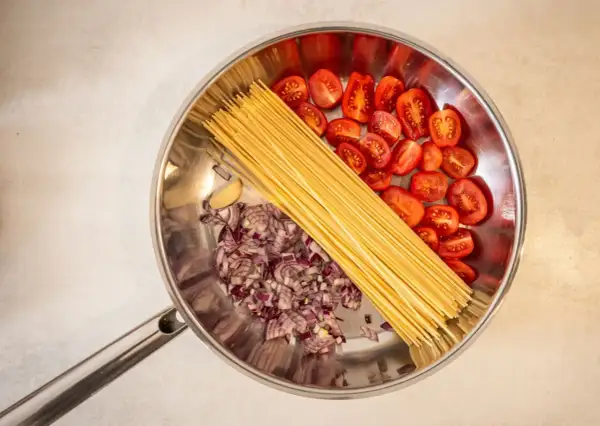 Zutaten für ein schnelles One-Pot-Gericht: Spaghetti, gehackte rote Zwiebeln, Kirschtomaten und Knoblauch in einer Pfanne.