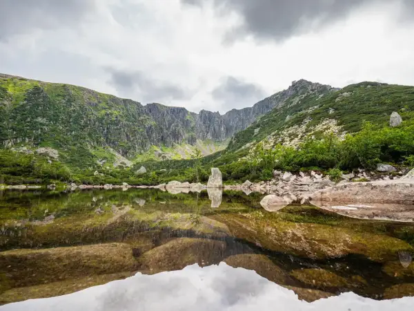 Spokojne, górskie jezioro odbija skaliste zbocza i chmury. To widok z najkrótsza trasa do Śnieżnych Stawków.