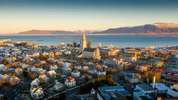 Fakta om Island: Reykjaviks ikoniska kyrka Hallgrímskirkja reser sig över staden med havet och snöklädda berg i bakgrunden.