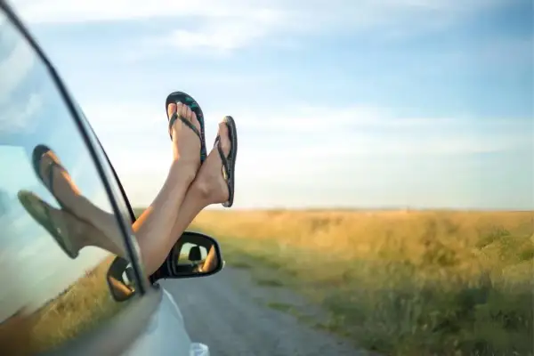 Pieds en claquettes sortant de la fenêtre d'une voiture, profitant du voyage par une journée ensoleillée.