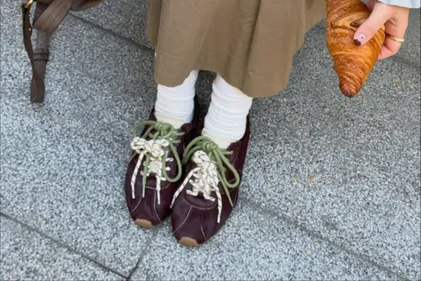 Modne sneakersy 2026 w bordowym kolorze, z zielonymi i białymi sznurówkami, idealne na spacer z croissantem.