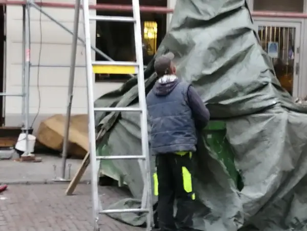 Pracownik w kamizelce i czapce przykrywa coś zieloną plandeką. Czy to hałas?