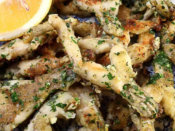 Un plat de cuisse de grenouille frite, garni de persil frais et d'ail, servi avec un quartier de citron.
