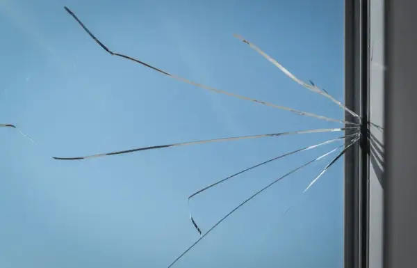 Pęknięte szkło okienne, przypominające pajęczynę, z widocznym niebieskim niebem w tle. To nie jest węgarek, tylko uszkodzone okno.