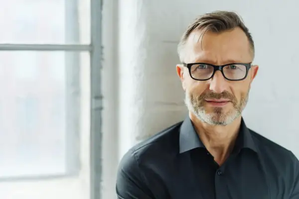 Man med glasögon och skägg, klädd i svart skjorta. Perfekt för bra profilbilder som ger ett professionellt intryck.