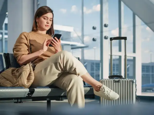 Junge Frau mit Handy in der Airport Lounge, Koffer daneben.