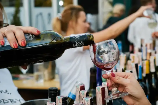 Rödvin hälls upp i ett glas, perfekt vin till lutfisk. Bakgrunden visar en festlig sammankomst med fler vinflaskor.
