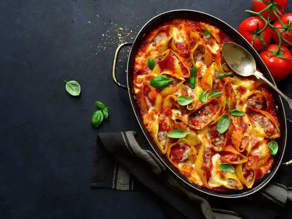 Conchiglioni farcis à la sauce tomate et au fromage, prêts à faire lever la pâte au four. Garnis de basilic frais.