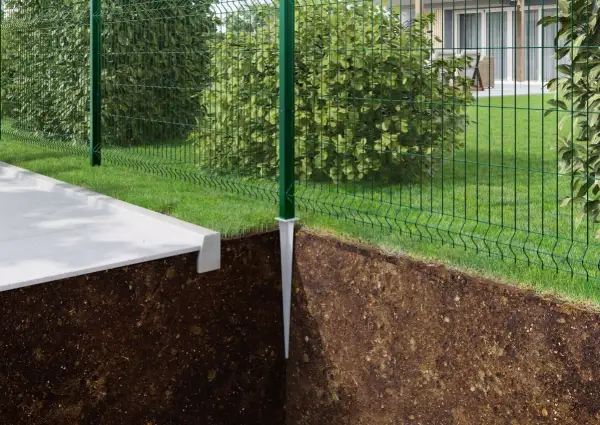 Montaż słupków ogrodzeniowych instrukcja: zielony słupek z metalową stopą wbity w ziemię, obok betonowy chodnik i siatka ogrodzeniowa.