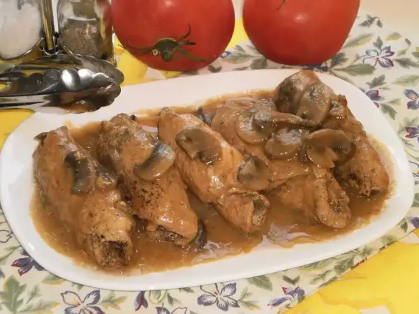Pyszne gołąbki z pieczarkami w sosie, podane na białym talerzu. Obok stoją pomidory i przyprawniki.