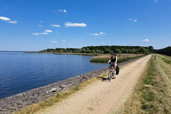 Kobieta na rowerze przemierza malownicze trasy rowerowe opolskie wzdłuż jeziora.
