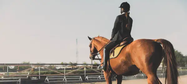 Une cavalière en tenue d'équitation, le périnée bien soutenu, monte un cheval brun dans une carrière.