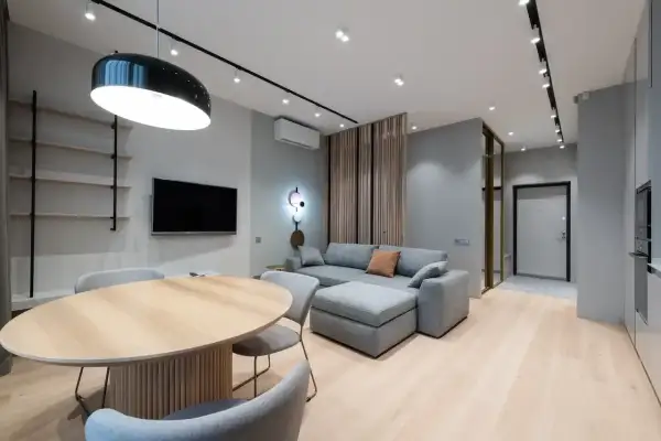 Nowoczesny salon z szarą kanapą i drewnianym stołem. Ściany w odcieniu cool white, jasna podłoga.