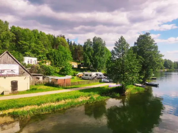 Malowniczy widok na jezioro i lasy, gdzie leżą Bory Tucholskie. Kemping z kamperami i łodziami przy brzegu.