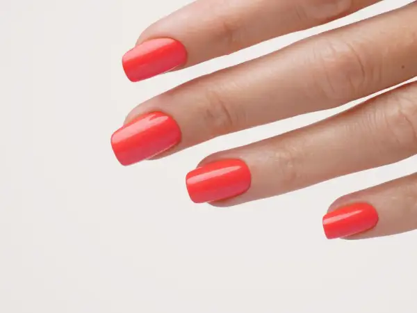 Main d'une femme avec un vernis corail vif, parfait pour un ongle vacances.