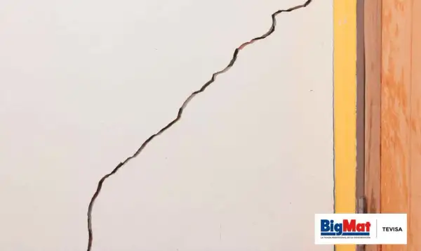 Grieta profunda en pared blanca, junto a marco amarillo y puerta de madera. Guía para saber como arreglar grietas profundas en paredes.