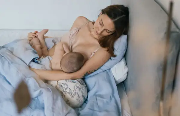 Matka w wygodnej pozycji biologicznej do karmienia, przytulona do poduszki, karmi piersią swoje dziecko.