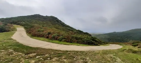Camino serpenteante en Serra do Cando, rodeado de vegetación verde y marrón bajo un cielo nublado.
