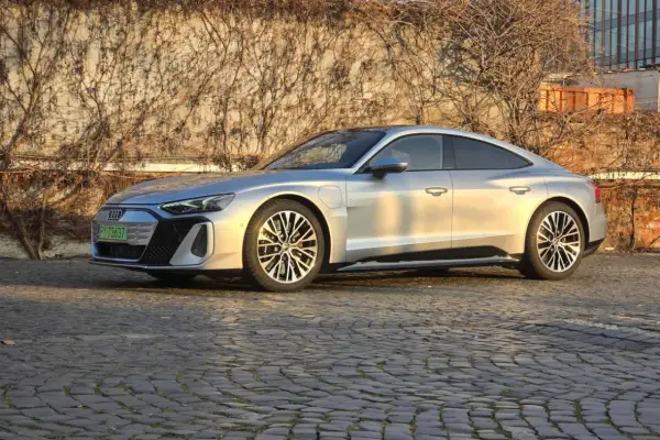 Srebrny Audi e-tron GT lśni w słońcu na brukowanej ulicy, z pnączami na ścianie w tle.