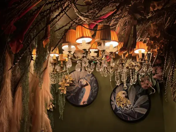 Décor luxuriant et excentrique d'un restaurant insolite à Paris, avec des lustres ornés, des plantes suspendues et des tableaux d'oiseaux exotiques.
