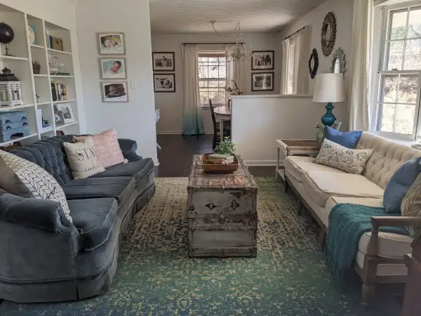 A living room with two sofas, a vintage trunk coffee table, and a patterned rug. This space shows how to brighten a dark room with light-colored furniture and ample natural light.