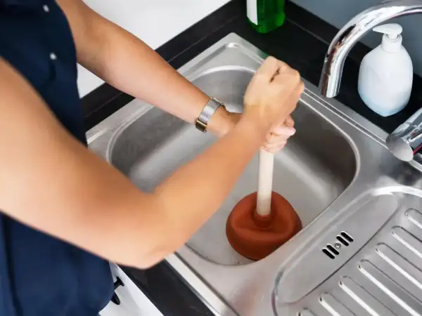 Une personne utilise une ventouse pour déboucher la canalisation d'eau chaude de l'évier.
