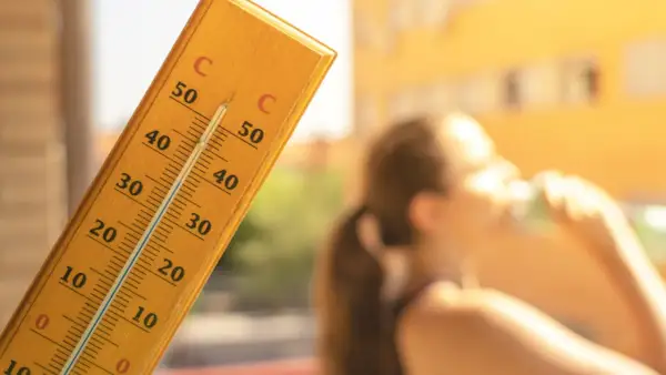 En termometer visar över 30 grader. En person dricker ur ett glas. Frågan är hur varmt får det vara på jobbet?
