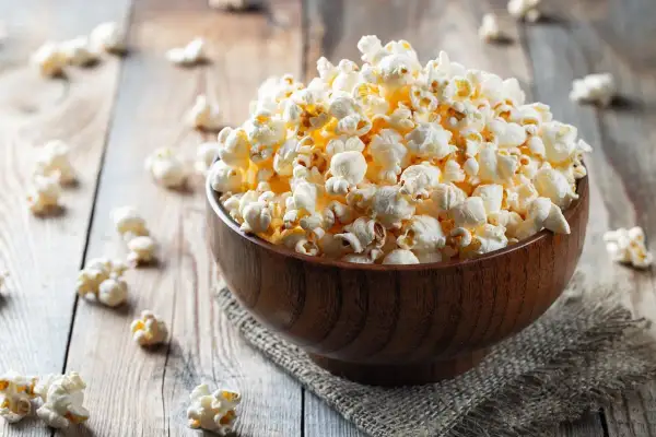 Drewniana miska pełna karmelowego popcornu na drewnianym tle.